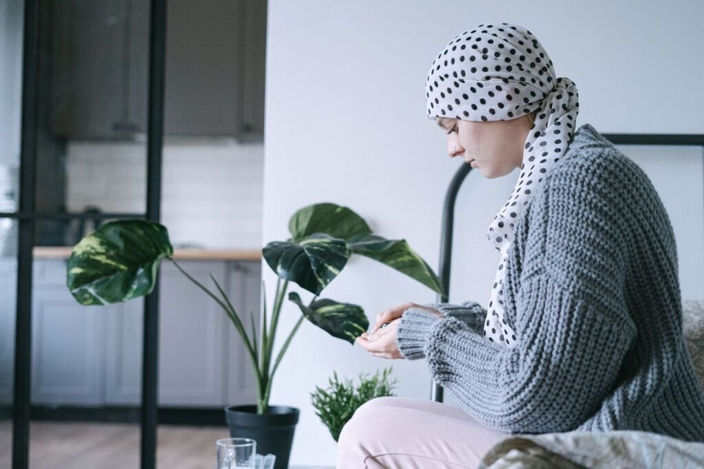 pexels-photo-6436268-6436268 Woman in headscarf sitting indoors, taking medication, symbolizing cancer care and support.